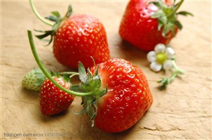 新鲜水果-在木质桌子上的三颗新鲜草莓及花朵