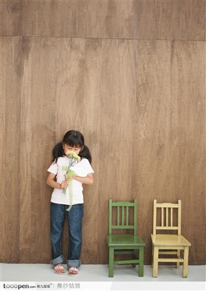 靠着墙边的一个拿花的小女孩和两把椅子