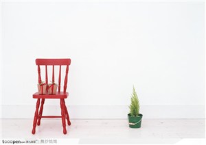一把红色木椅子上的两个礼品盒与地板上的一盆圣诞树幼苗