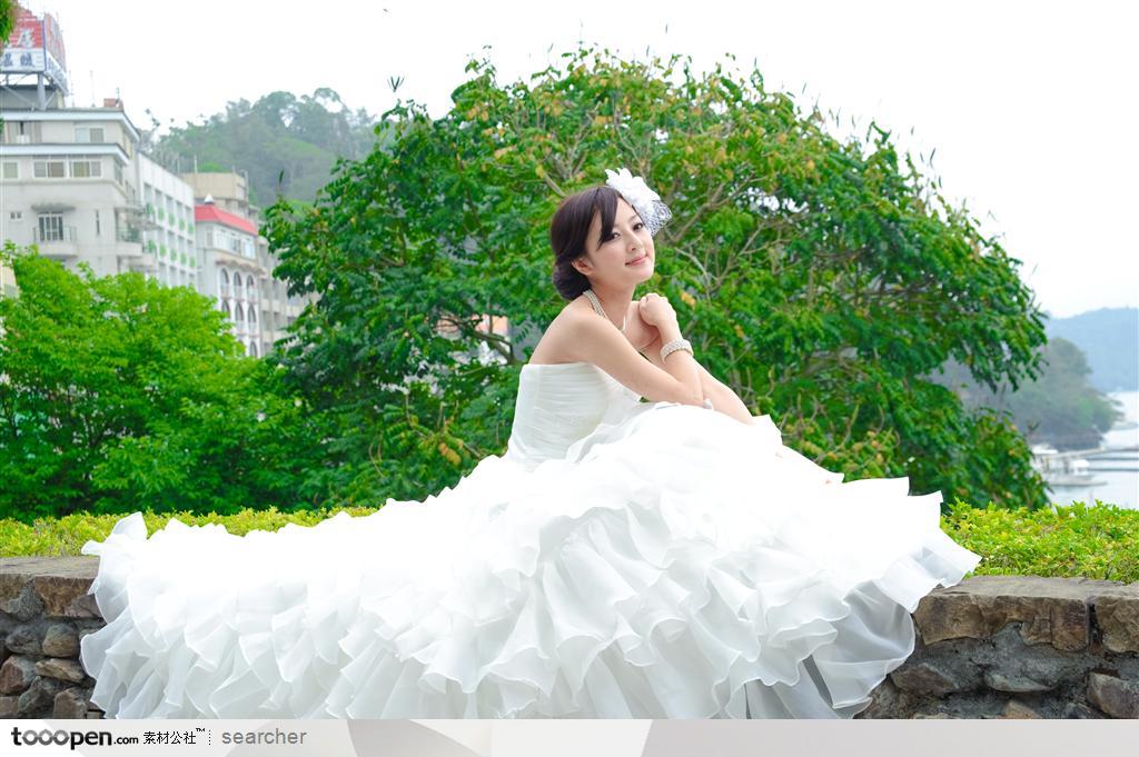 坐在墙上穿白色婚纱礼服的美女新娘