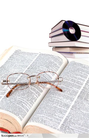 放在摊开的英语字典上的眼镜和靠着一摞书的光碟