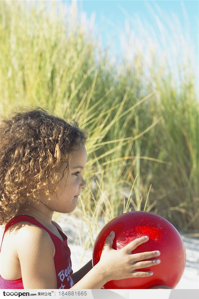 坐在沙滩上手里拿着红色球的小女孩