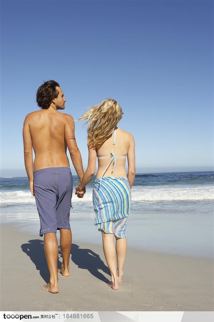 夫妻两手拉手在海边的沙滩上散步