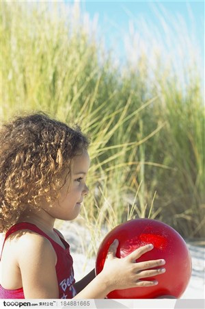 坐在沙滩上手里拿着红色球的小女孩