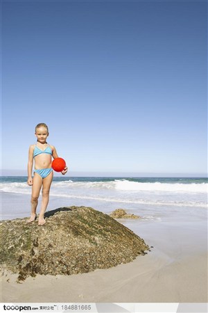 站在海边礁石上拿红色球的小女孩