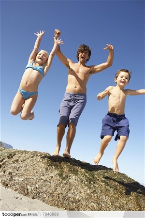 家庭海滩游-在沙滩的礁石上往下跳的爸爸和孩子