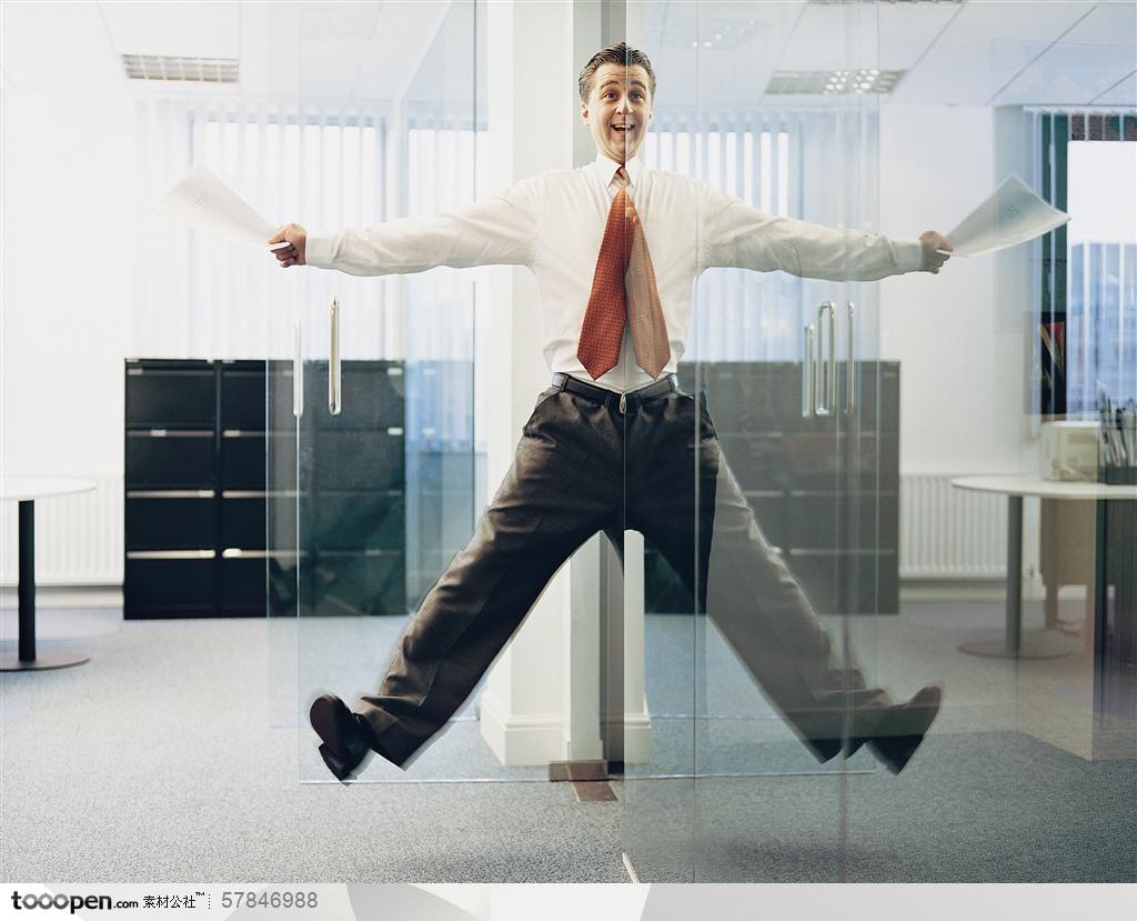 商务百态创意-拿着文件再玻璃房办公室门口跳跃的外国职场男士