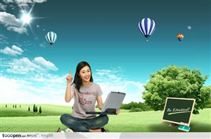 盘腿坐在绿色草地上抱着笔记本电脑的女性和草地上的小黑板