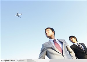 雄心勃勃的年轻人-两个穿西装的职场男士微笑的仰望着天空飞过的飞机