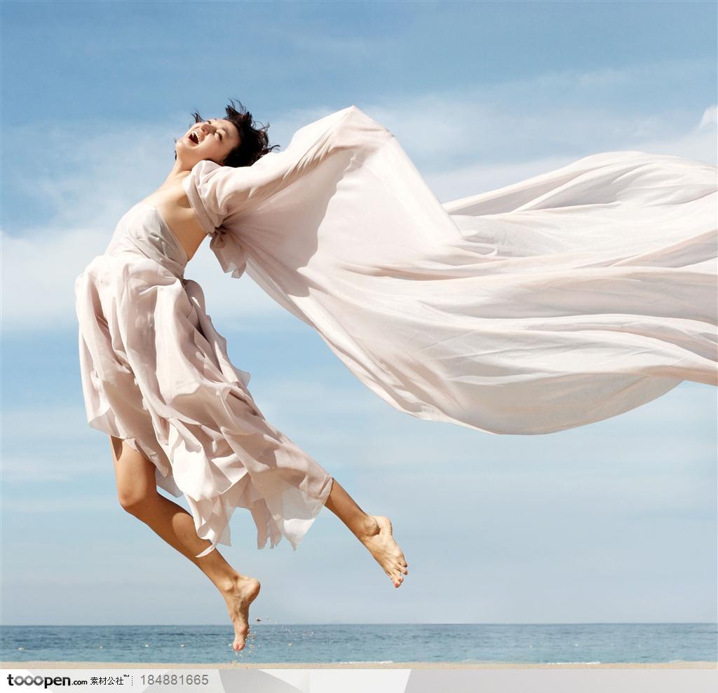 穿白色抹裙飘扬的披肩在沙滩上跳跃