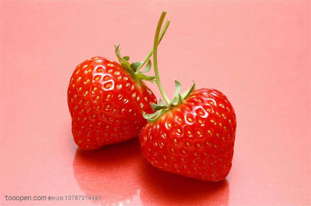 新鲜水果-在红色背景前的两颗新鲜草莓