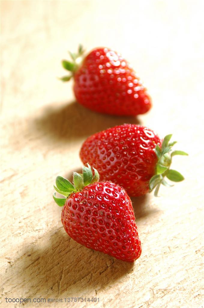 新鲜水果-在木头桌面上的三颗新鲜草莓水果图片