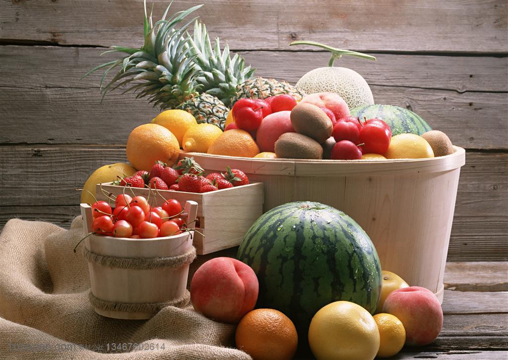 新鲜水果-木质桌子的麻布袋上摆着木质桶子里面摆放着苹果、西瓜、草莓、樱桃、菠萝等新鲜水果