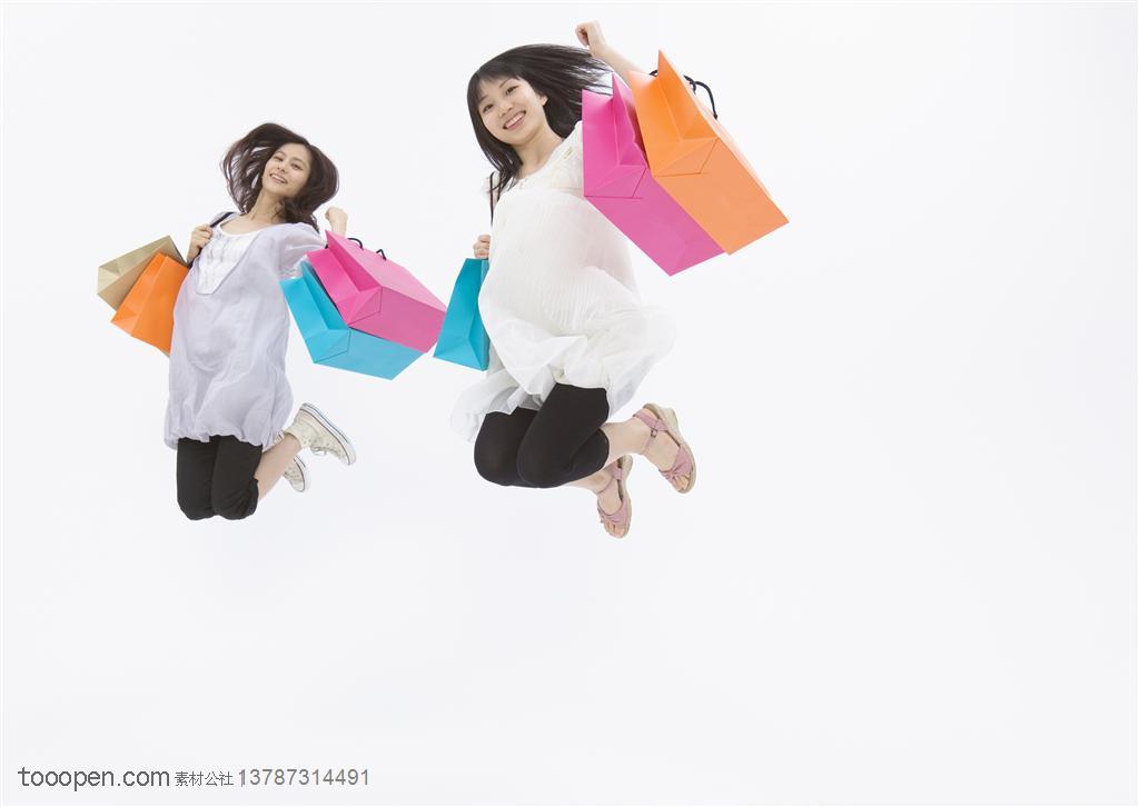 青春活力-两个女孩提着购物袋跳跃在空中
