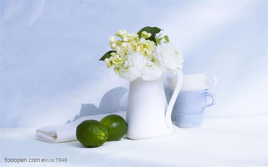 家俱饰品-白色花瓶里的花朵和边上摆放的两个青柠檬