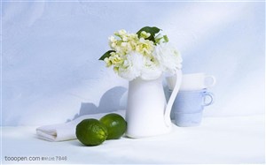 家俱饰品-白色花瓶里的花朵和边上摆放的两个青柠檬