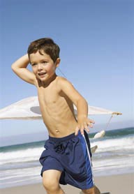 家庭海滩游-举着风筝奔跑在海边的外国小男孩